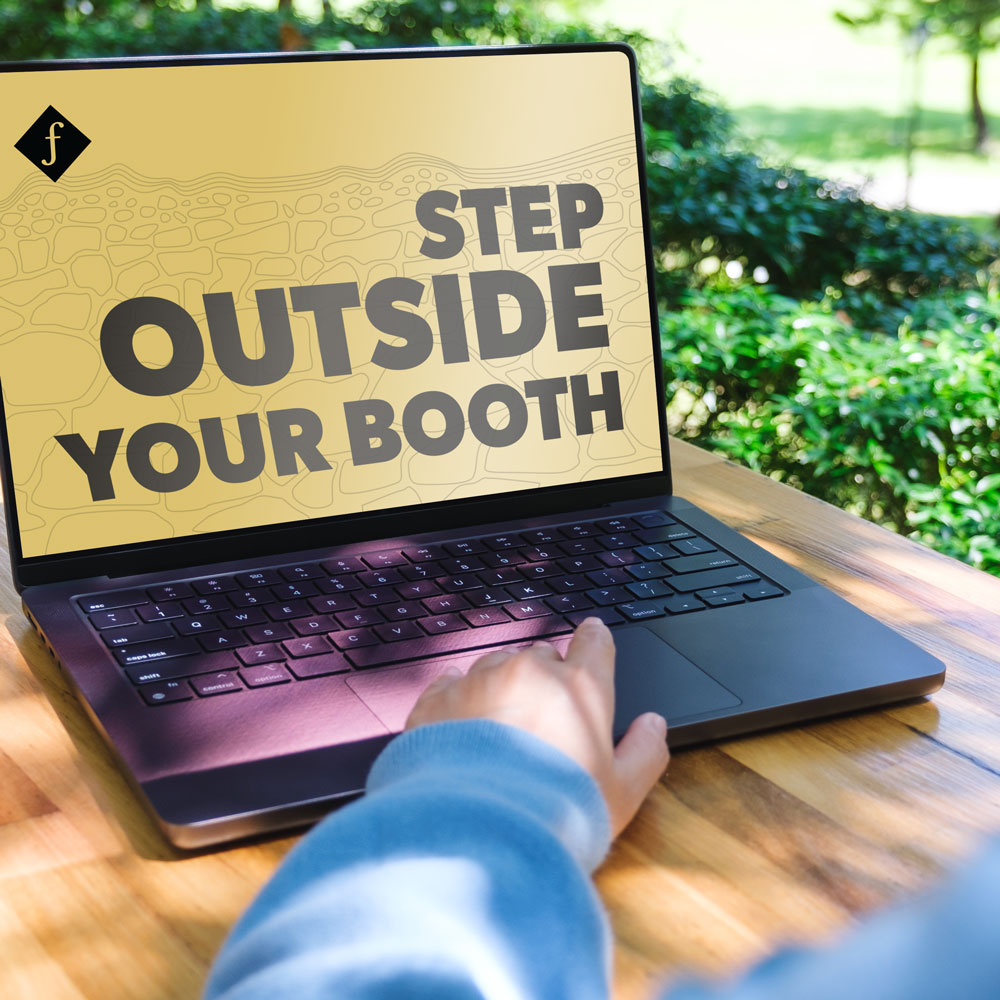 Person working on a laptop at an outside table with trees in the background